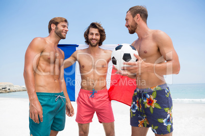 Portrait of man holding French flag while standing with male friends at beach