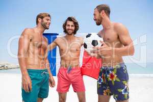 Portrait of man holding French flag while standing with male friends at beach