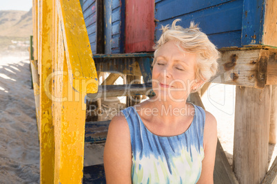 Close up of senior woman with eyes closed sitting by hut at beach