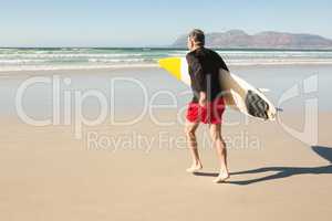 Rear view of man carrying surfboard while running on sand