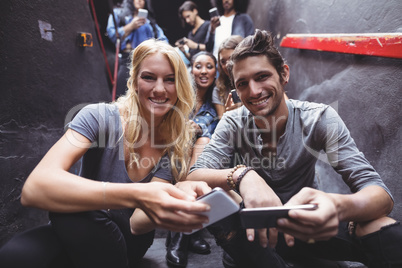 Portrait of happy friends using mobile phones on steps at nightclub