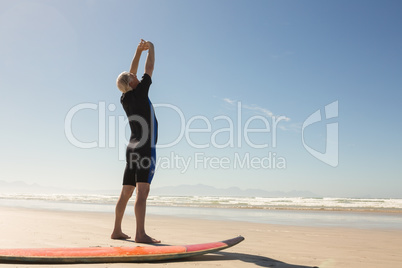 Rear view of man exercising while standing by surfboard