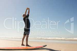 Rear view of man exercising while standing by surfboard
