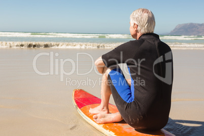 Rear view of senior man sitting on surfboard against sea