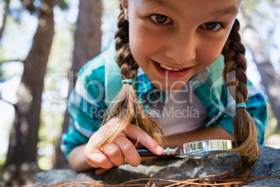 Smiling girl using magnifying glass in the forest
