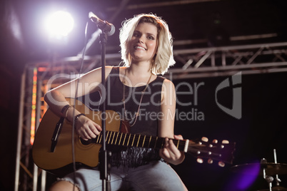 Portrait of smiling female guitarist playing guitar at nightclub