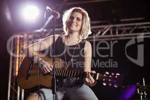 Portrait of smiling female guitarist playing guitar at nightclub