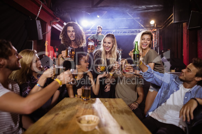Cheerful friends toasting drink at table with performer singing on stage