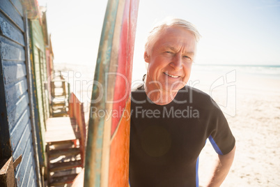 Portrait of smiling senior man standing by surfboard