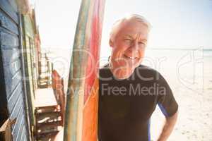 Portrait of smiling senior man standing by surfboard