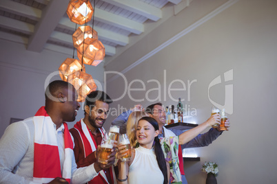 Group of friends toasting glasses of beer while watching match