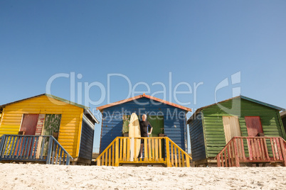 Man standing with surfboard at beach hut