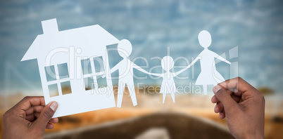 Composite image of hands holding a family with her house in paper