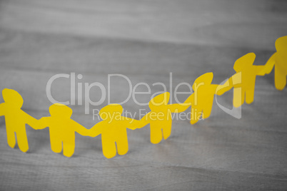 Paper cut out figures forming chain on wooden table
