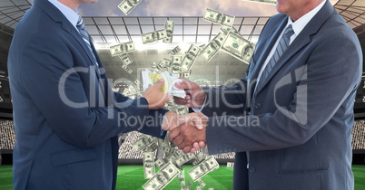 Midsection of businessmen exchanging money while shaking hands on soccer field representing corrupti