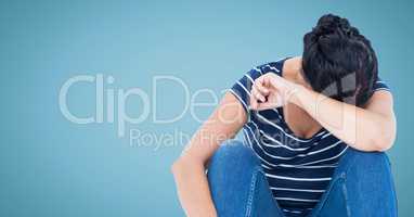 Woman sitting and crying into arm against blue background