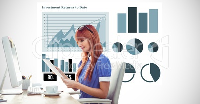 Redhead woman holding document at computer desk against graphs