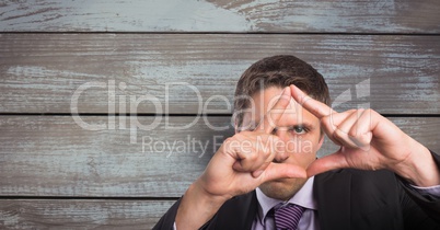 Portrait of businessman looking through hands against wooden wall