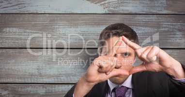 Portrait of businessman looking through hands against wooden wall