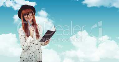Smiling redhead woman holding book against sky