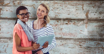 Portrait of smiling businesswomen with digital tablet against wooden wall