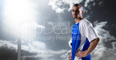 Portrait of confident soccer player with hand on hip against sky