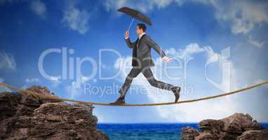 Businessman with umbrella walking on rope