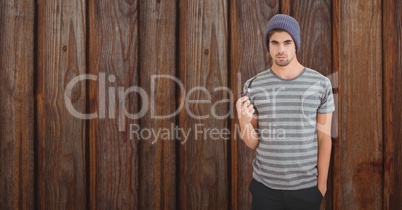 Portrait of young man holding tobacco pipe against wooden wall