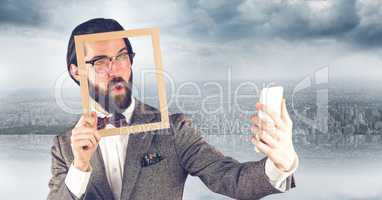 Hipster holding frame while taking selfie on mobile phone