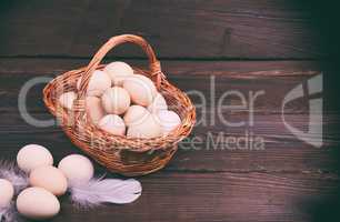 Raw chicken eggs in a wicker basket on a wooden surface