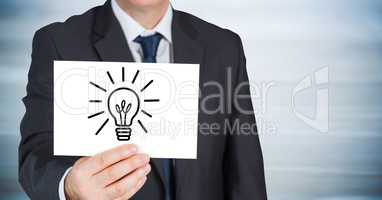Business man with lightbulb doodle on card against blurry blue wood panel