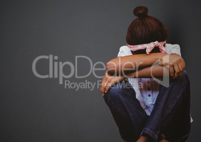 Girl with head between knees against grey wall
