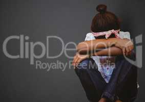 Girl with head between knees against grey wall