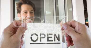 Hands photographing open sign through transparent device while man smiling in coffee shop