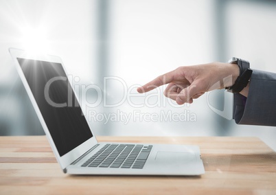 Hand pointing at laptop against blurry grey office with flare