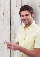 Portrait of happy male hipster holding smart phone against wooden wall