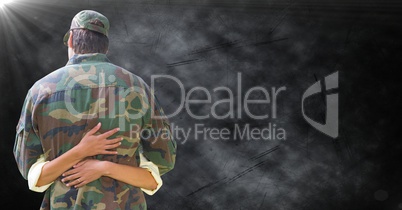 Back of soldier being hugged against black grunge background with flare