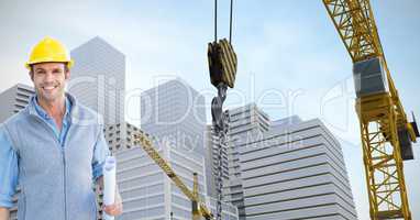 Smiling architect holding blueprints by crane against buildings