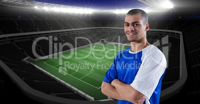 Smiling soccer player with arms crossed against stadium