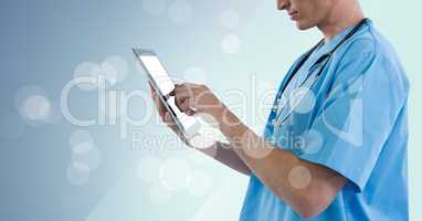 Doctor mid section touching tablet with bokeh against blue background