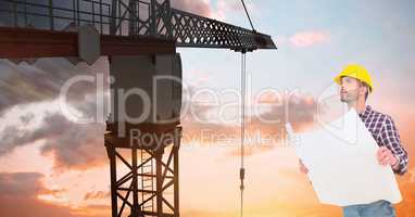 Architect holding blueprint while looking at crane against sky during sunset