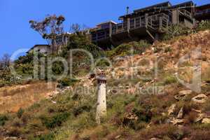 Goats cluster along a hillside with homes and a tower in Laguna