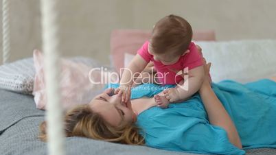Joyful mother playing with her baby infant in bed