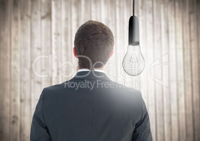 Back of Business man with glowing lightbulb against blurry wood panel