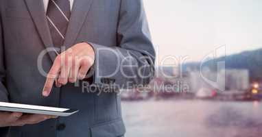 Business man mid section with tablet against blurry skyline and red overlay