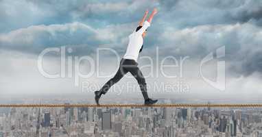 Businessman with arms raised walking on rope against cityscape
