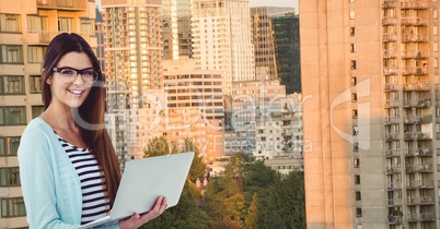 Smiling businesswoman holding laptop against buildings
