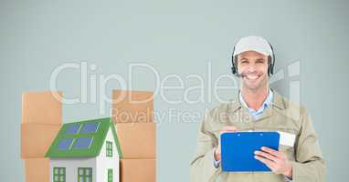 Smiling delivery man holding clipboard by house and parcels