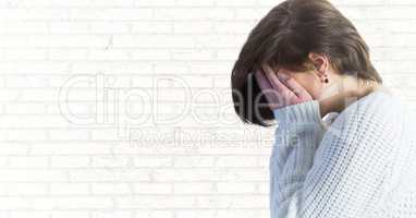 Woman profile with hands over face against white brick wall