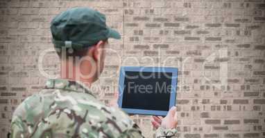 Back of soldier with tablet against brown brick wall